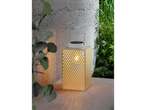 An illuminated lantern with a perforated pattern stands on a surface next to a plant.