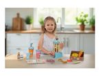 Young girl playing with a wooden toy blender, fruit, and smoothie cups on a kitchen table.