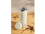 Garrafa térmica creme com tampa e grãos de café numa mesa de madeira.