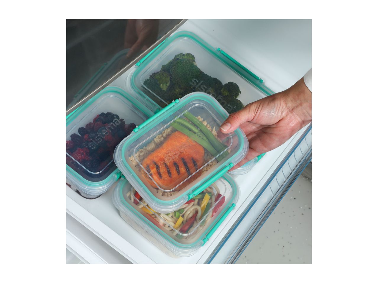 A hand placing a plastic food storage container with salmon and vegetables into a refrigerator.