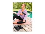 Woman in a lilac hoodie and black joggers using a massage gun by a pool.