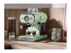Light green espresso machine with two espresso cups, coffee beans, and milk on a wooden counter.