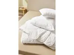 Piumino e cuscini bianchi trapuntati piegati su un letto color crema.