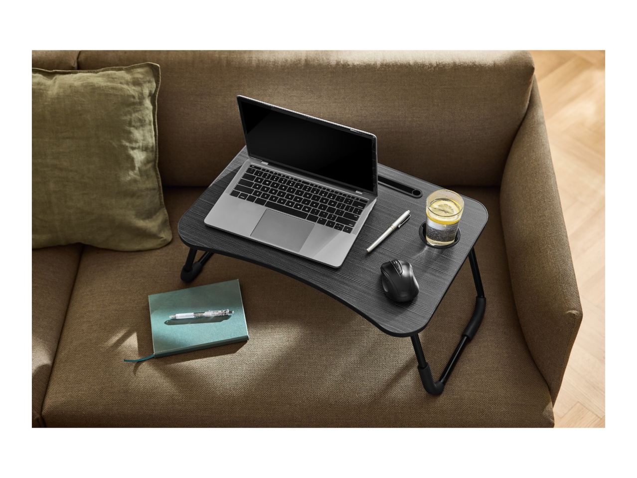 Laptop table with a laptop, mouse, pen, and drink on a sofa with a cushion.