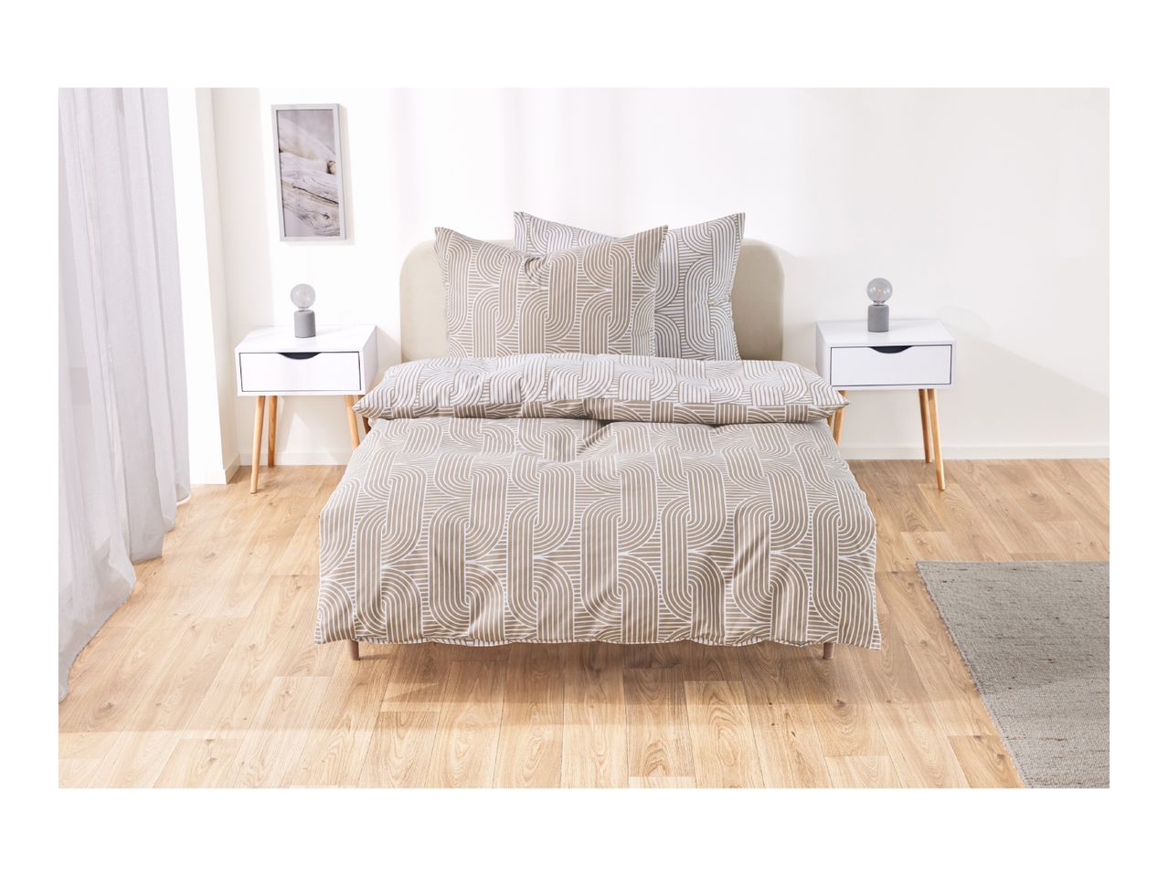Bedroom with a bed featuring beige and white patterned duvet cover and pillows, two white nightstands with lamps, and a framed picture.
