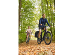 Two people cycling on electric bikes with pannier bags through an autumn forest.