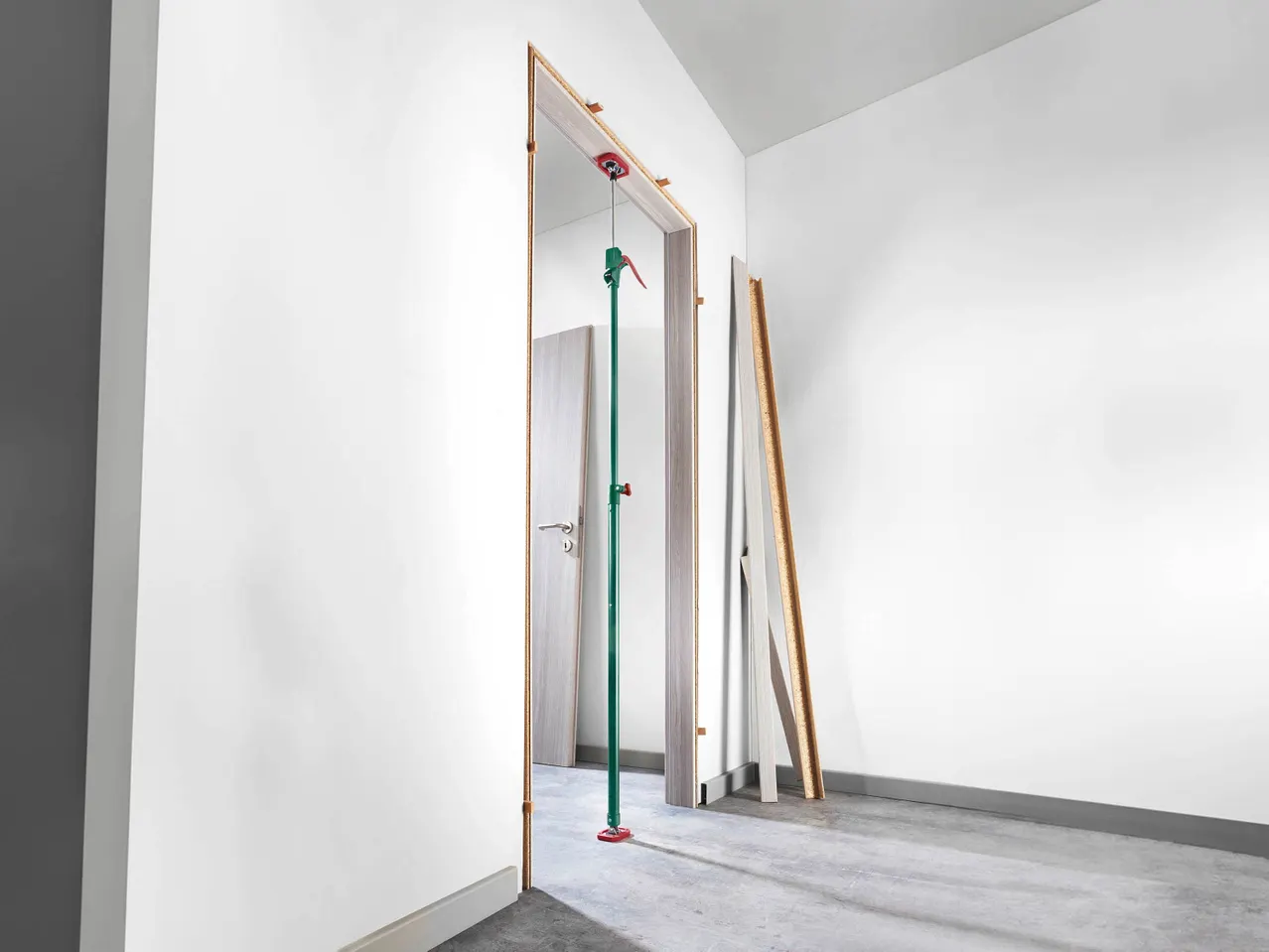 A green and red Ceiling Support Rod holds a door frame in place during installation.