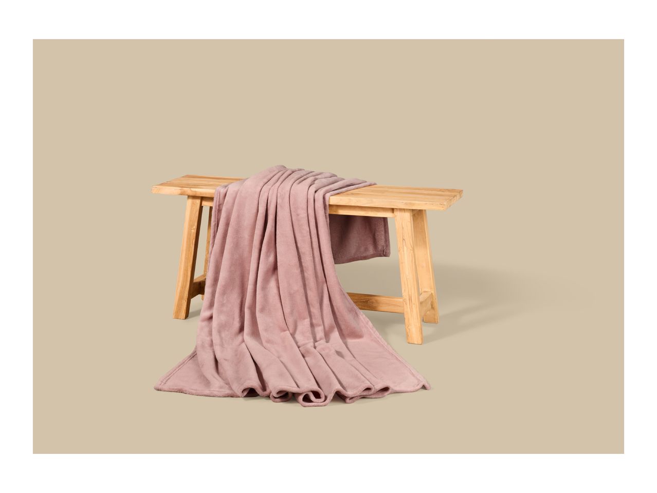 A soft pink fleece blanket draped over a rustic wooden bench.
