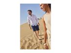 Man in white linen shirt and shorts, woman in beige top walking barefoot on sand dunes.
