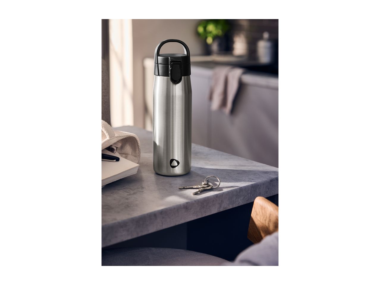 Stainless steel water bottle on a kitchen counter with keys and a notebook.