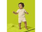 Toddler in a cream-colored muslin shirt and shorts set, standing on a green mat.