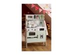 A child's play kitchen with a microwave, oven, sink, and refrigerator, decorated with festive bunting.
