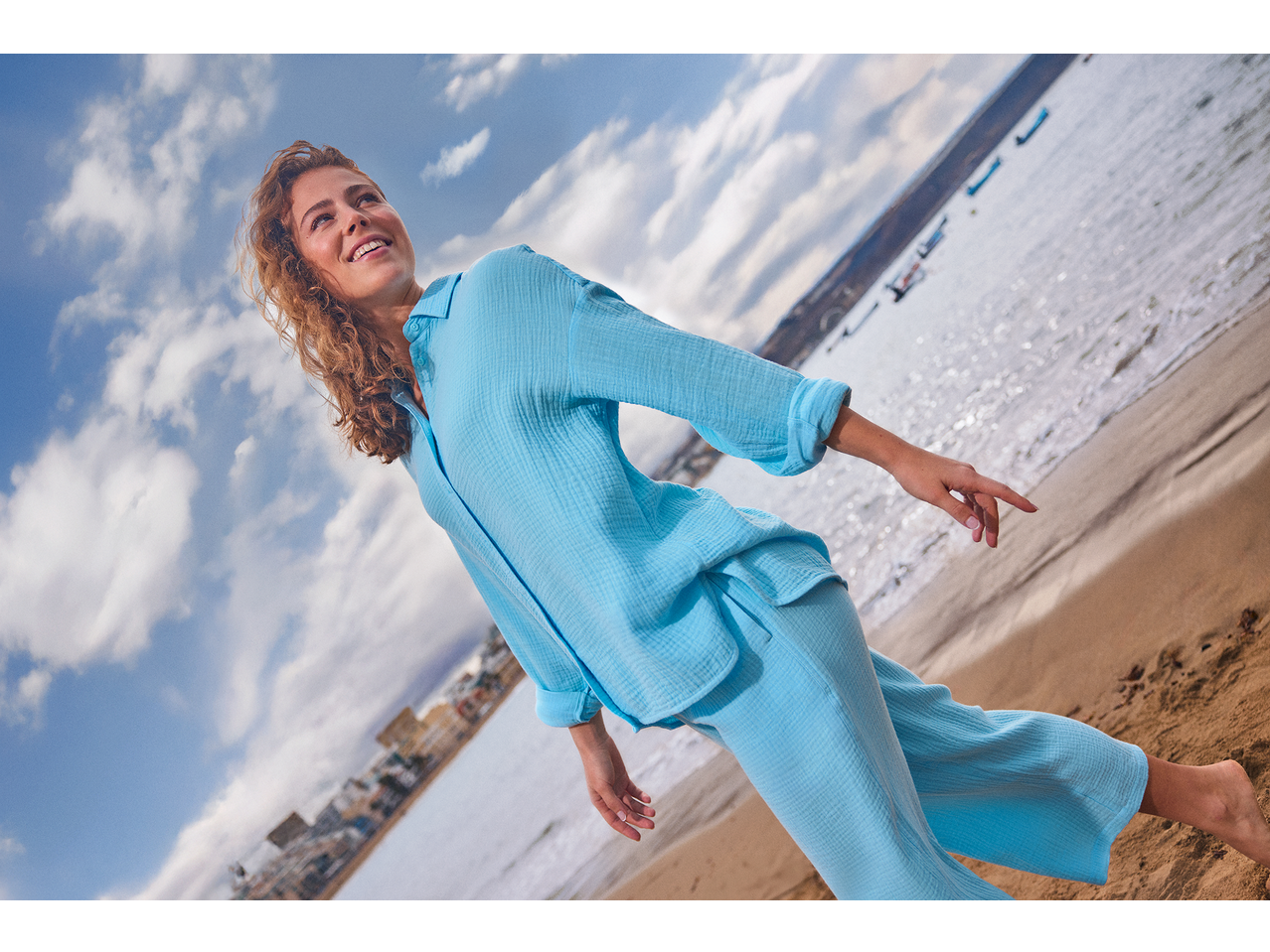 Femeie zâmbitoare în cămașă și pantaloni de muselină ESMARA, pe plajă.