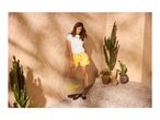 Woman in white top and yellow shorts holding a straw bag with 'Playa' text, surrounded by cacti.