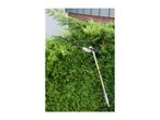 Long-reach hedge trimmer cutting a green hedge in front of a house.