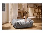 A small dog resting in a plush grey pet bed on a wooden floor.