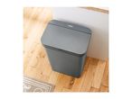 A grey Tower brand step bin sits on a light wood floor.