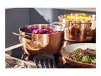 Copper pots and pans with food cooking on a black induction hob