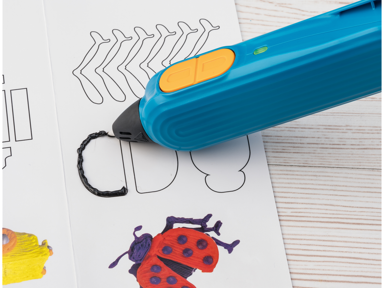 3D писалка CRELANDO рисува с черен цвят върху бял шаблон с мотив на калинка.