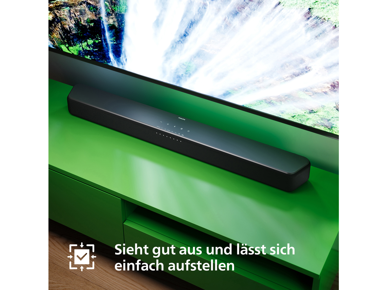 Philips Soundbar 2.0 auf grünem TV-Möbel vor einem Fernseher mit Wasserfallbild.
