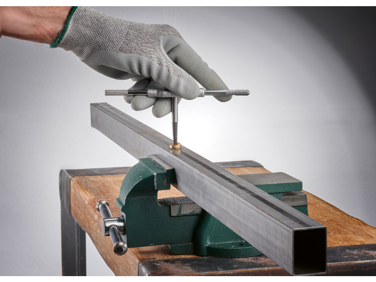 Mănușă de lucru gri, menghină verde și profil metalic, cu o cheie de filetat