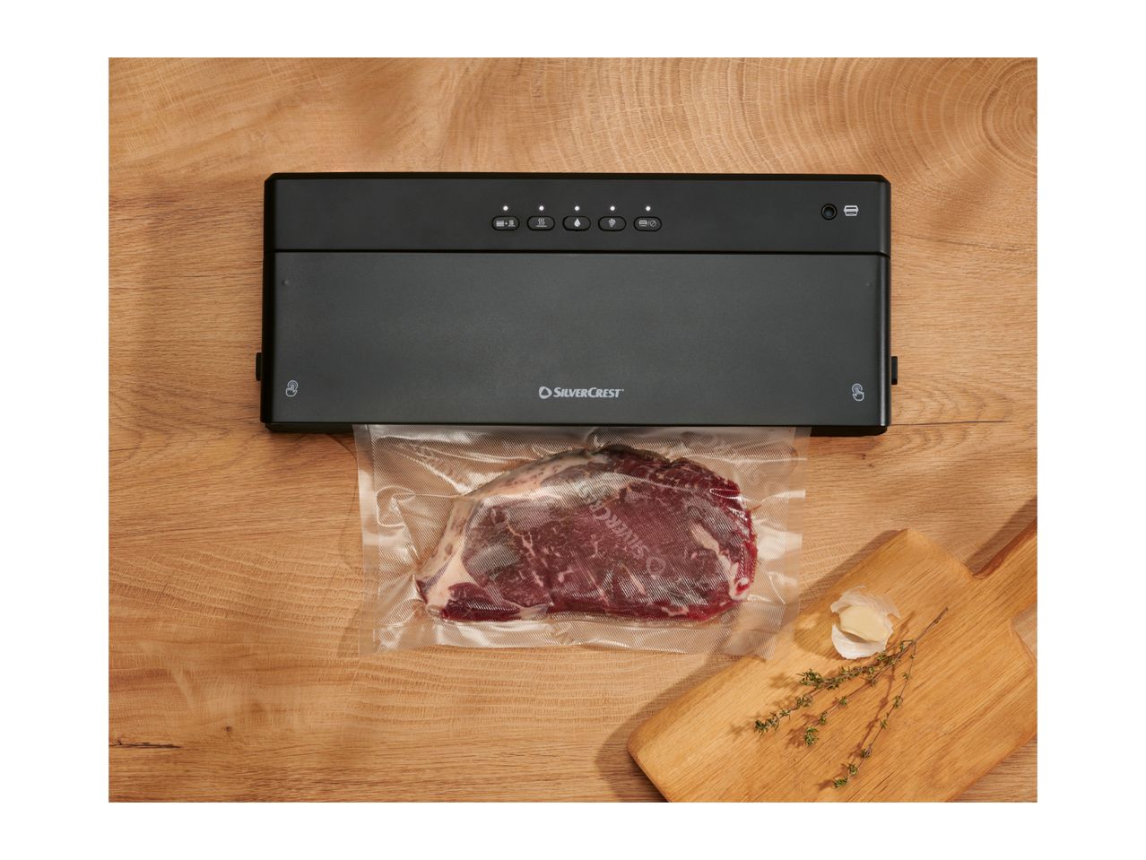 A black vacuum sealer packaging a piece of meat on a wooden surface.