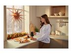 A woman using a compact food chopper in a cozy, festively decorated kitchen.
