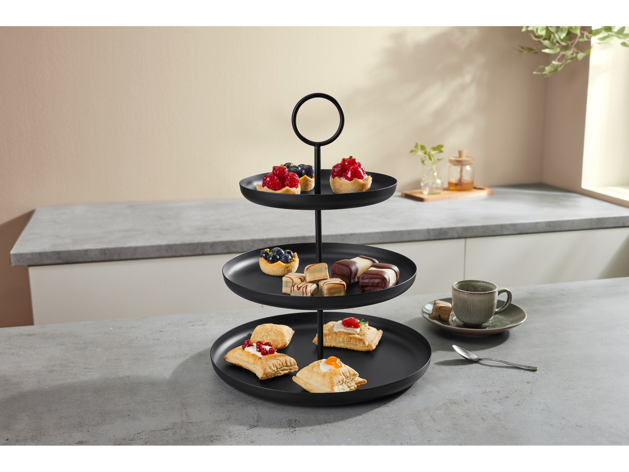 Black three-tier stand with pastries and a coffee cup on a kitchen counter
