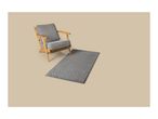 Grey armchair with wooden frame and a grey rug with a geometric pattern on a beige background.