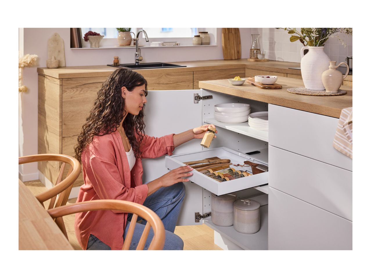 A woman organizing spices in a modern kitchen cabinet drawer.