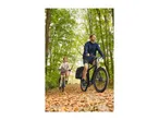 Two people cycling on a path covered with autumn leaves in a forest.