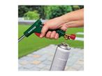 A person holding a gas weed burner, preparing to attach it to a gas canister in a garden setting.
