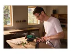 Man using a bench grinder with a flexible shaft attachment to work on wood in a workshop.
