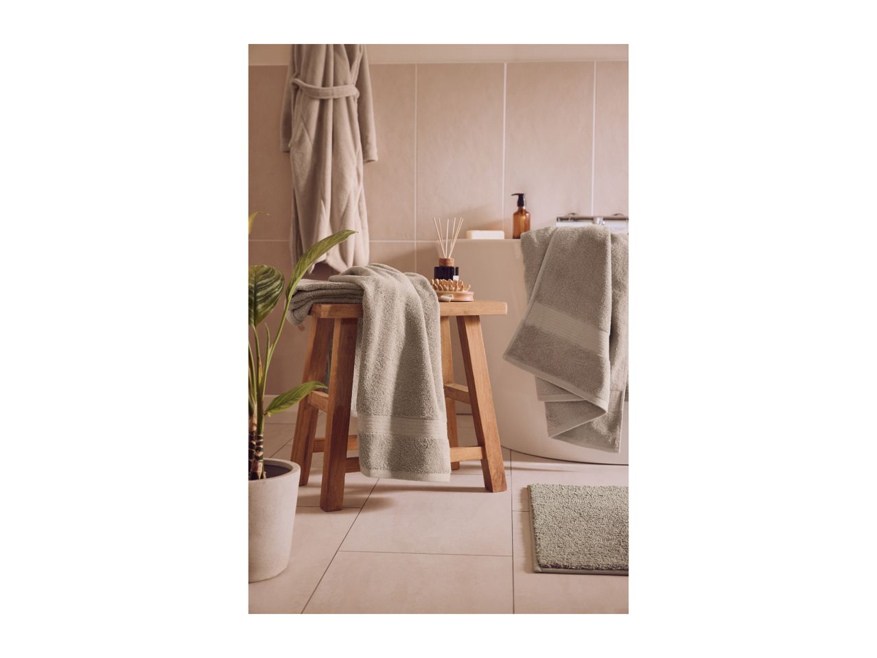 Bathroom with light grey towels on a wooden stool and hanging over a bathtub.