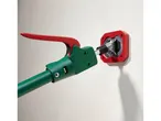 A green and red tool with a handle connected to a red wall-mounted device.