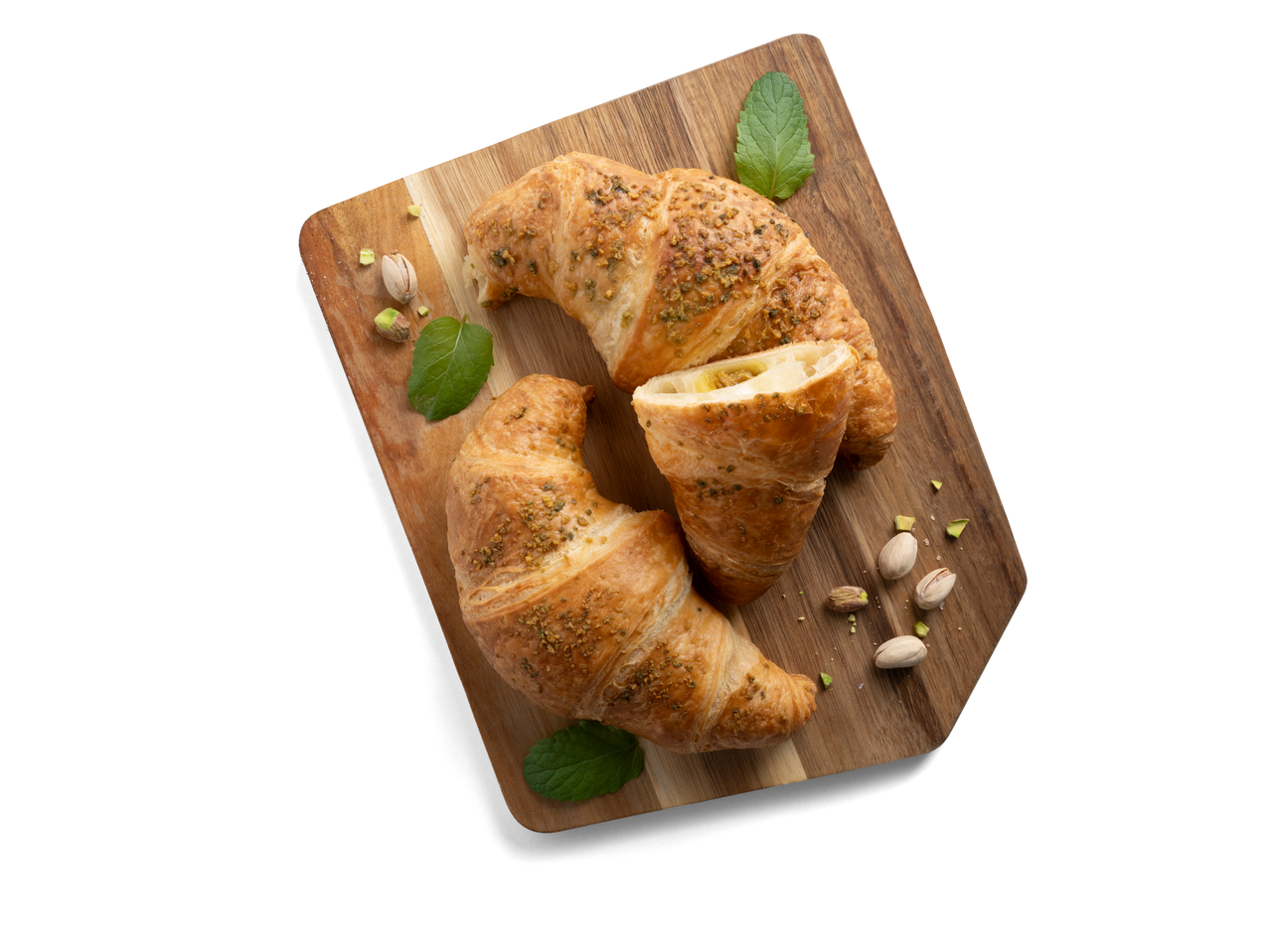Két pisztáciás croissant vágódeszkán, pisztáciával és mentával díszítve.
