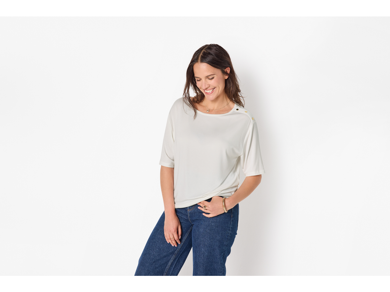 Femeie într-un top alb cu mânecă scurtă și blugi albaștri, zâmbind