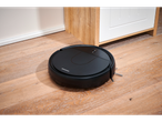 SILVERCREST® Robot Vacuum Cleaner on a light wooden floor next to a white cabinet.