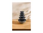 Stack of five glass bowls with black lids on a wooden surface.