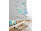 A three-tiered clothes drying rack with clothes hanging on it, next to a laundry basket.