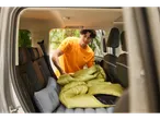A man puts a sleeping bag and inflatable mattress in the back of an SUV.