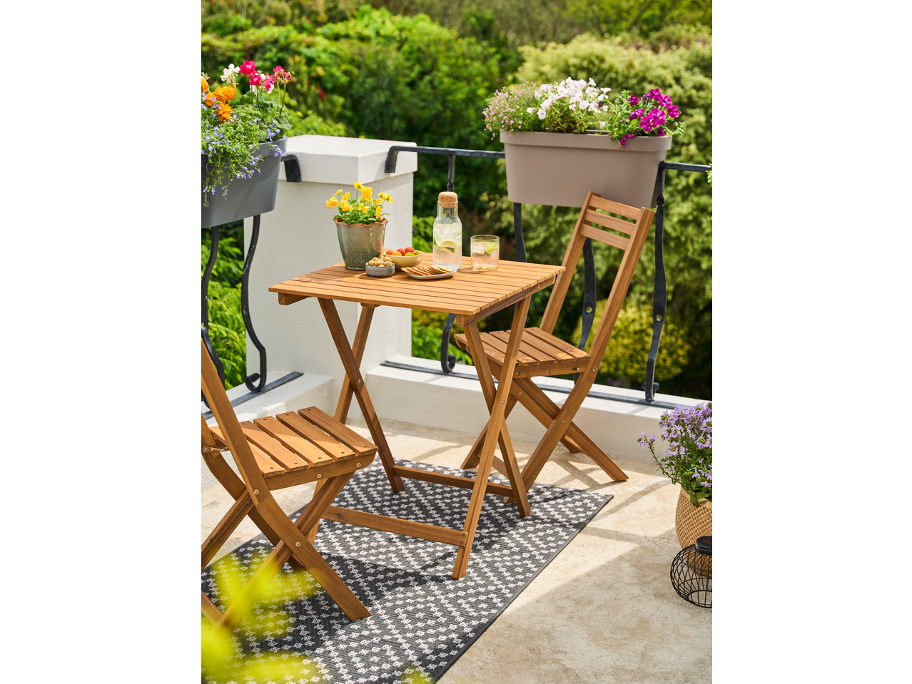 Set bistro din lemn pentru balcon, cu gustări și băuturi, înconjurat de flori în ghivece.