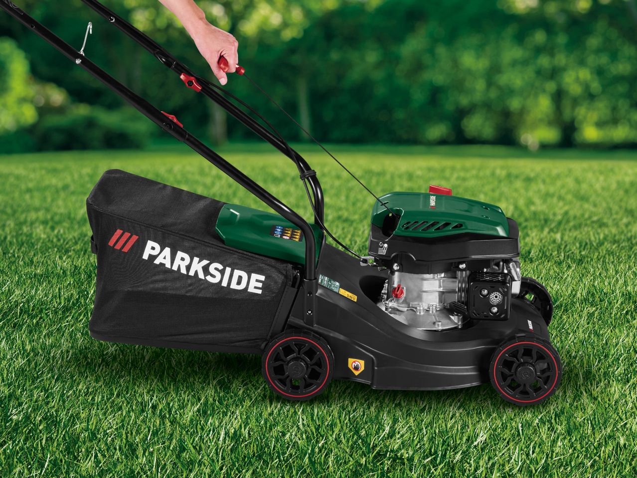 Person operating a petrol lawnmower with a black grass collection bag on green grass.
