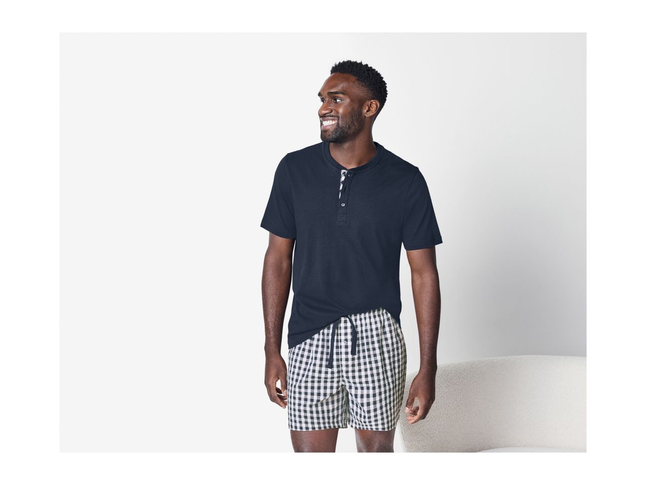 Man in a navy short-sleeved Henley shirt and black and white checkered shorts.