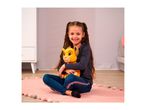 A smiling girl with pigtails sits on a pink rug, hugging a yellow plush lion toy.
