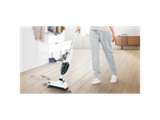 A person uses a Bosch cordless vacuum cleaner to clean paw prints from a wooden floor.