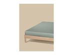 A light green fitted sheet on a wooden bed frame against a beige background.