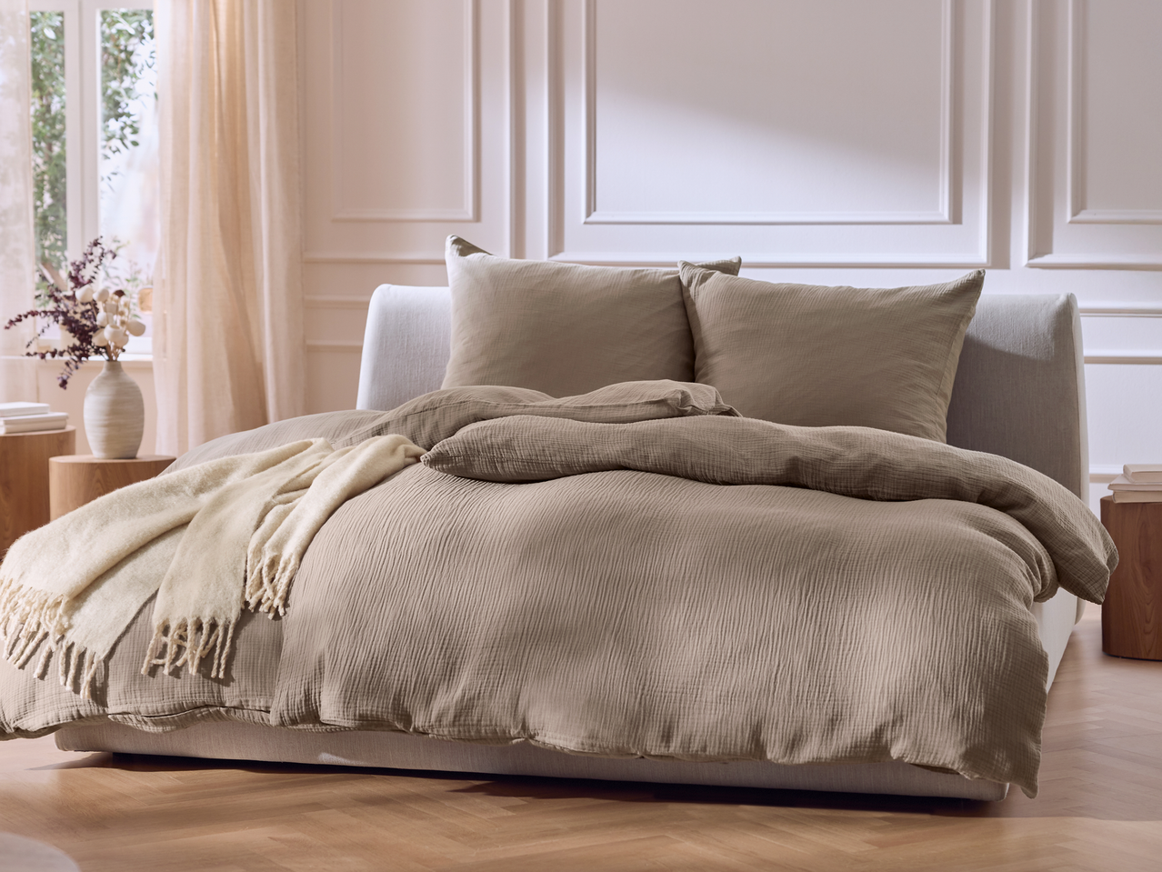 Υπνοδωμάτιο με κρεβάτι με μπεζ πάπλωμα, μαξιλάρια και κουβέρτα.