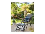 Garden chair and footstool with a cushion and notebook, with a woman in the background.