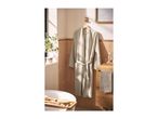 Light grey waffle bathrobe hanging on a wooden hook in a bathroom with a bathtub and wooden vanity.